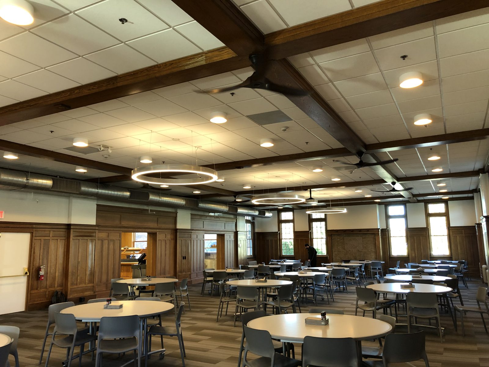 Dining hall with wood beams, ceiling fans and LED ring pendants at Tilton School